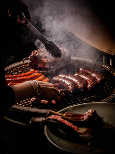 Person grilling sausages on a bstrd barbecue with smoke in the background