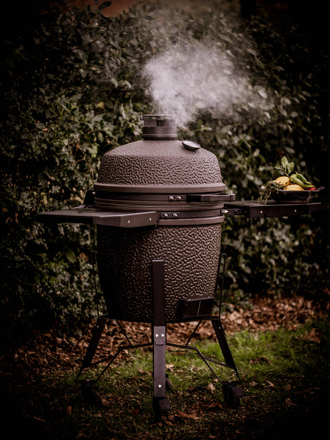 Outdoor bstrd kamado grill with smoke rising against a dark background